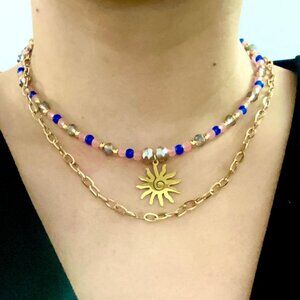 Layering necklace in gold, peach, and navy blue colors with a sun pendant